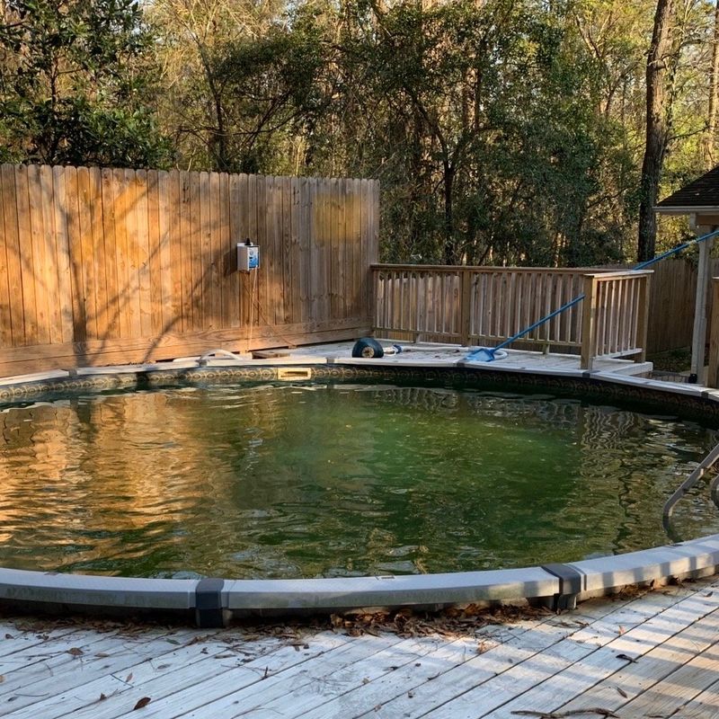 Round above-ground pool with a wooden deck, the water dark green
