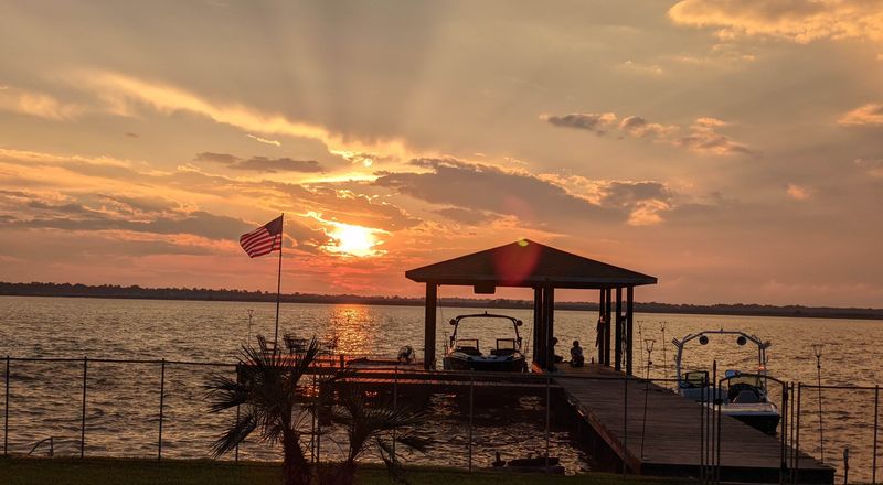 Sunset over Lake Houston with a boat dock, palm fronds and an American flag